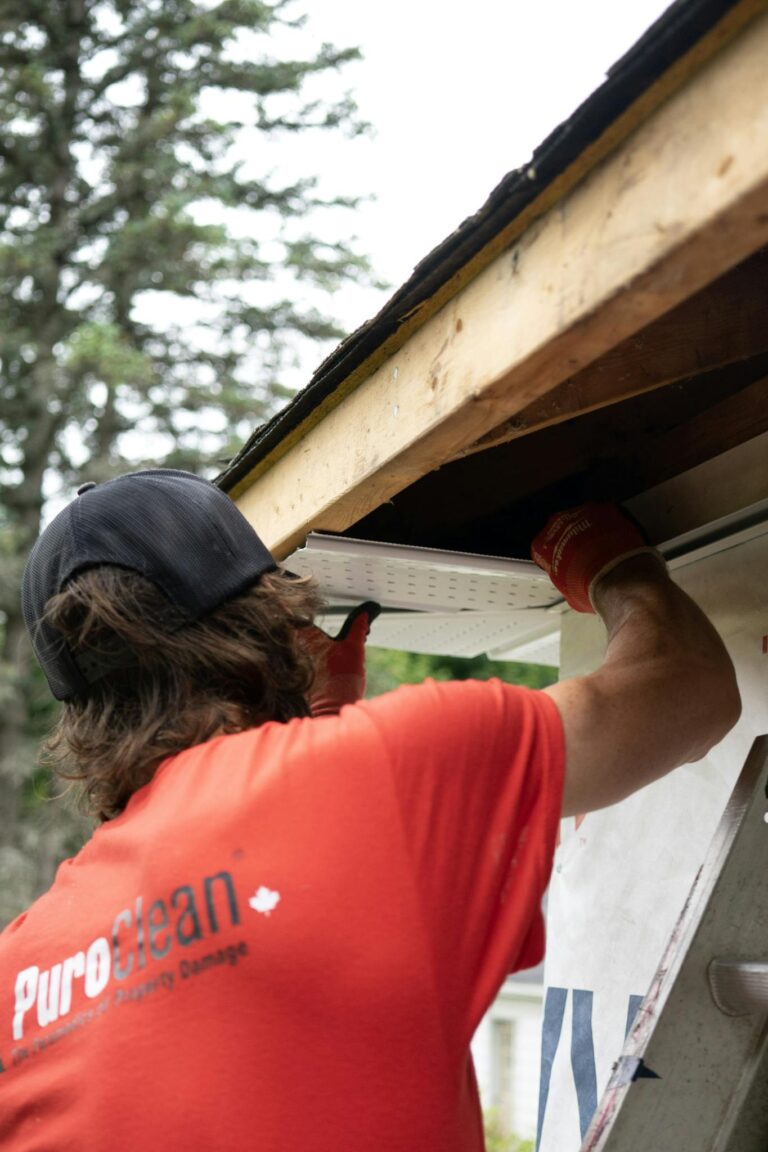 Construction worker in red shirt installing gutter under eaves, demonstrating roofing services and home maintenance.
