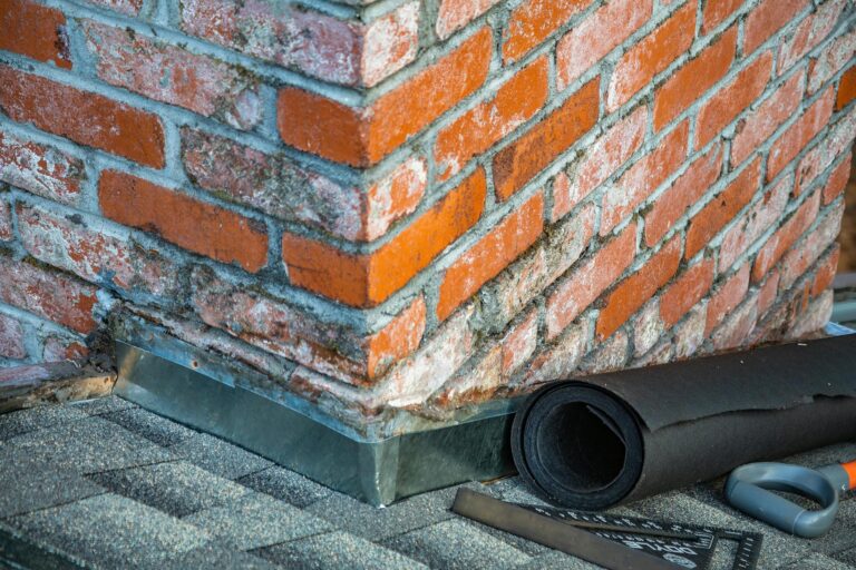 Detailed view of a brick chimney with visible mortar and metal flashing, showcasing roofing materials and tools, relevant to roofing services in Knoxville.