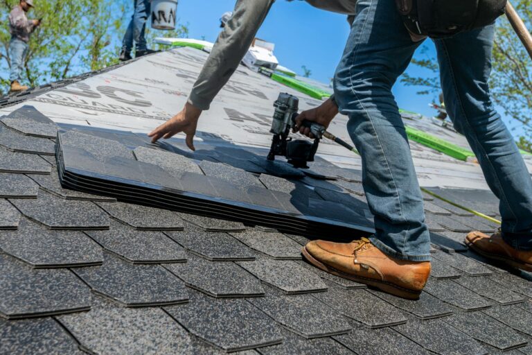 Roofer using a nail gun to install shingles on a sloped roof, demonstrating roofing services relevant to THP Roofing of Knoxville.