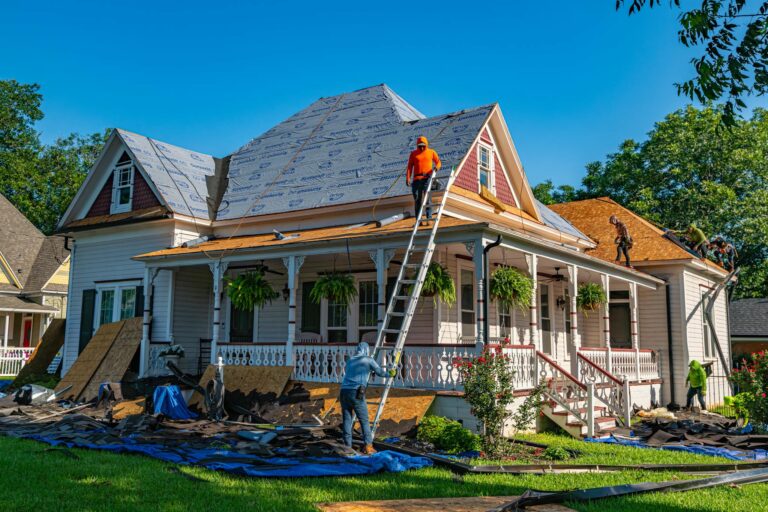 Roofers replacing a historic home's roof, with workers using ladders and scaffolding, surrounded by construction materials and tarps in Knoxville.