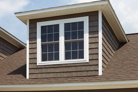 Window installation on a home featuring a stylish design with brown siding and a peaked roof, enhancing energy efficiency and curb appeal for residential properties.